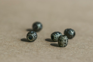 Five metal bronze beads close-up on craft paper in the sunlight. Materials for needlework and creativity.
