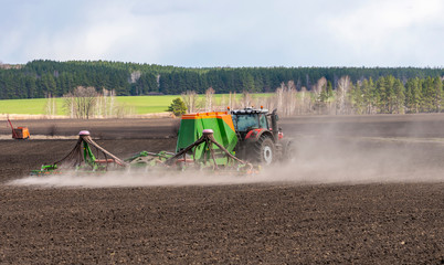 Spring field work, a tractor with a trailed seeder sows seeds in an agricultural field