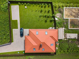 Aerial top view of house shingle roof with attic windows and black car on paved yard with green...