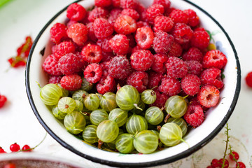 selection of freshly picked ripe red raspberries and gooseberry in enameled bowl