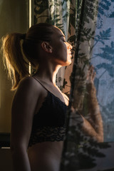 Obraz premium Young woman looking through curtains.