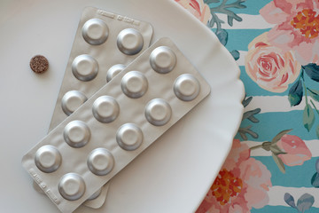 Iron pills on a plate. Many tablets of Ferrous sulfate. Supplement use for Iron Deficiency Anemia. Floral retro background. Pastel color.