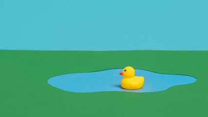 Stop motion animation of a single rubber duck ducky swimming in a pond and taking a dip to drink water or eat before leaving and shaking the water off and exiting the frame - Powered by Adobe