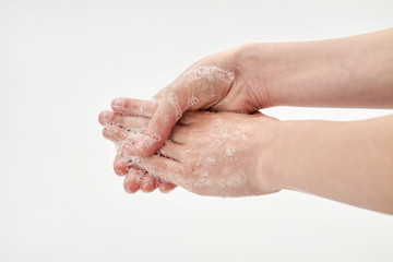 Fototapeta premium Coronavirus or Covid-19 concept. A small girl washing hands with soap. Process of hand washing with soap on white background. Closeup, selective focus