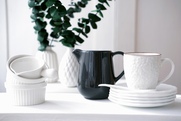 white cup, plates, saucer and milk jug on a white table. copy space for text. fresh and minimal kitchen style concept. clean and uncluttered room. scandinavian design. 
