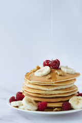 breakfast, pancakes with raspberry, nuts, banana and honey on a white plate
