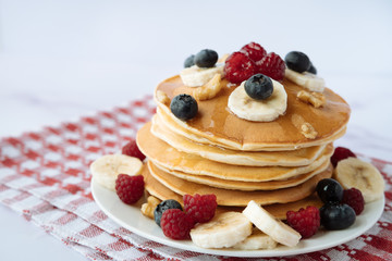 breakfast, pancakes with raspberry, blueberry, nuts, banana and honey on a white plate