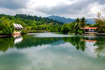 Fototapeta na wymiar Summer wooden bungalows ashore of the picturesque lake surrounded by a beautiful tropical park on tropical Koh Chang island in Thailand.