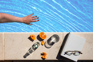 a hand into the water next to a white book with glasses and fruits 