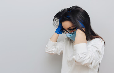 Young nurse doctor in a protective blue medical mask and glasses holds his head in his...