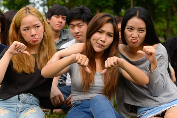 Stressed young group of friends giving thumbs down together at the park