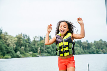 Happy, excited girl in life jacket on dock at lake