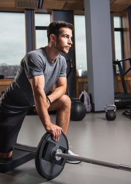 Fit young man working out with heavy weights standing on one knee pulling the barbell up