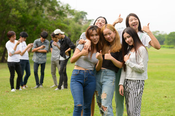 Happy young group of friends giving thumbs up together at the park