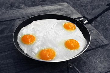 Old wooden table and frying pan with fried eggs on camping gas stove