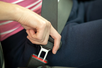 Close up of woman hand fastening seat belt while sitting inside a car for safety before driving on the road. Female driver driving secure and taking safe jorney.