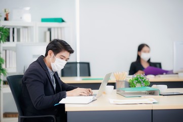 Fototapeta na wymiar Asian business people working in the office during the coronavirus or covid 19 spread in China and spread around the world. Employees must wear a medical mask and keep a distance to prevent infection.