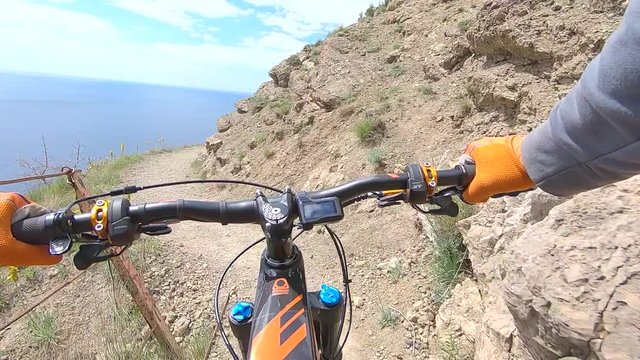 Point chest view from action camera bicycle handlebar and hands while riding on cliff edge trail along sea. Bicyclist holding handle wheel while riding on rocky mountain route on enduro mtb bike