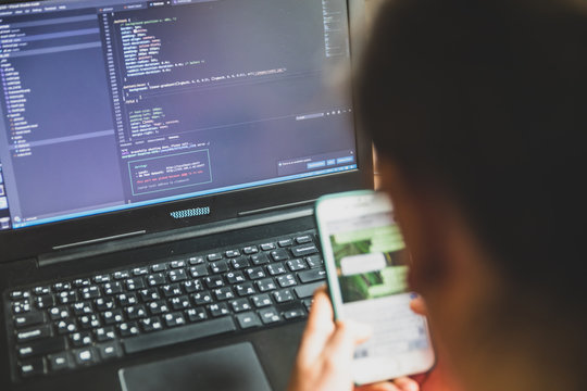Young caucasian girl in pink sweater at computer while studying online programming at home near the window