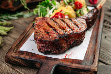 Closeup view on roasted grilled appetizing juicy steak with vegetables salad on the wooden board, horizontal format