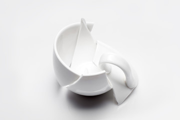 broken white ceramic tea cup on a white background, conceptual photo with a shattered object.