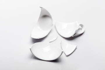 broken white ceramic tea cup on a white background, conceptual photo with a shattered object.