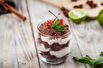 Tiramisu puff dessert with cream and chocolate in a glass decorated with cheeries ant mint leaves on the wooden table, horizontal format