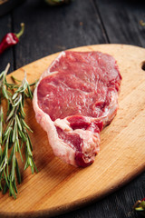 Top view closeup on piece of fresh raw meat for cooking steak with sprigs of rosemary on a wooden board, vertical