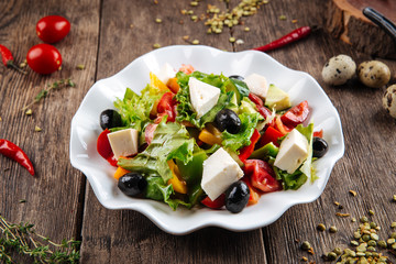 Side view on healthy greek salad with fresh vegetables, cheese and olives in a white plate on the wooden table, horizontal format