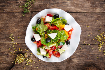 Top view on healthy greek salad with fresh vegetables, cheese and olives in a white plate on the wooden table, horizontal format