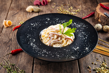 Side view on pasta carbonara in a black plate on the wooden table, horizontal format