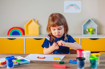 Beautiful toddler girl molding colorful clay on the table in the kids room