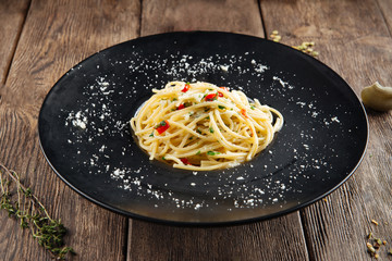 Side view on spaghetti aglio olio in a black plate on the wooden table, horizontal format