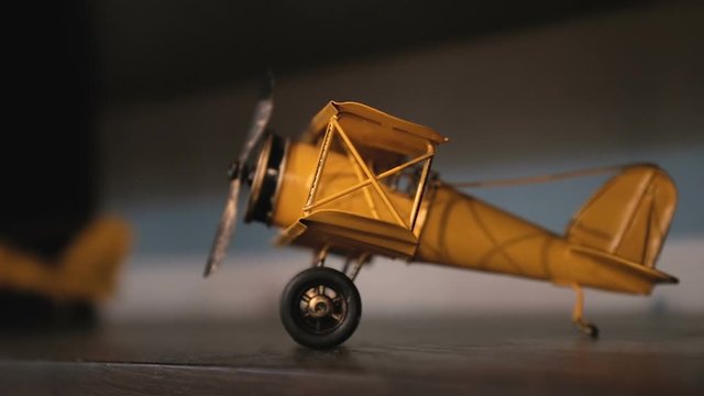 Miniature metallic airplane toy on a wooden shelf. Close up on childhood decorative toys. Panning left with revealing. Selective focus.