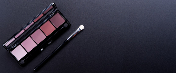 Cosmetic palette with brushes lies on a black background
