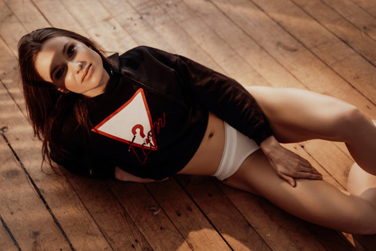 Attractive and sportive young woman looking hot wearing black hoodie and undies, posing in a soft sunlight of the apartment, while laying on the floor