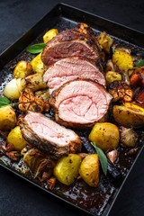 Traditional roasted veal roll roast offered with potatoes, carrots and onions as closeup on a metal sheet