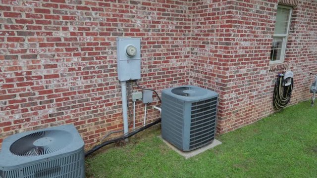Camera moves around to view two air conditioner units next to brick house