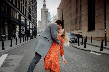 Fototapeta premium tourist couple in big city. The guy with the girl is hugging and happy. Girl in red dress kissing boy.
