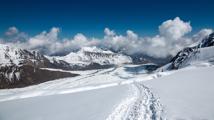 Fototapeta na wymiar Snowy deserted trail overlooking the mountain peaks in the clouds, against the blue sky