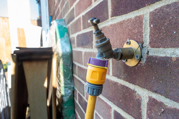 An outdoor garden tap with a hosepipe attached.