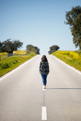Obraz premium Woman walking on the middle of a road in beautiful yellow flowers landscape in Alentejo, Portugal