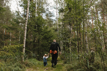 Obraz premium Back view of father and one-year-old daughter walking hand in hand in forest