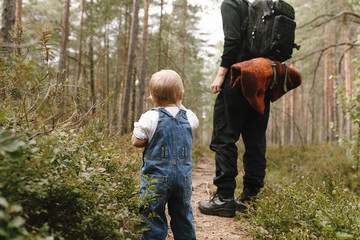 Back view of young toddler standing behind her dad in the forest on a late summer afternoon