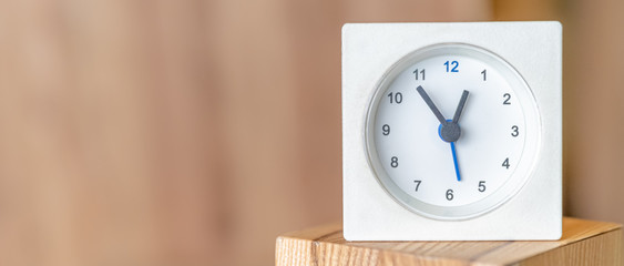 White clock on a wooden surface. Blurred wooden background. Copy space