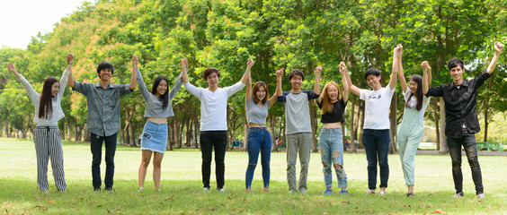 Happy young group of friends with arms raised together at the park