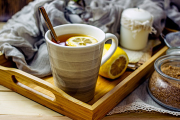 Obraz na płótnie Canvas Hot black tea with a slice of lemon in a large gray mug with a spoon closeup, top view, next to dried oranges, fresh lemon, brown sugar, gray napkin on a wooden tray. The concept of a cozy home tea 