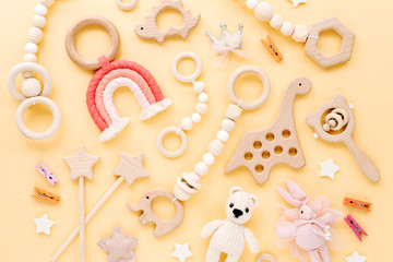 Cute wooden baby toys on yellow background. Knitted bear, rainbow, dinosaur toy, beads and stars. Eco accessories,  beanbag and teethers for newborn. Flat lay, top view