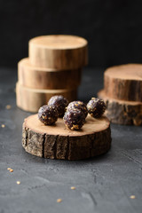Raw vegan sugar free sweets. Small energy balls with green buckwheat and nuts served on wood slab on black background angle view