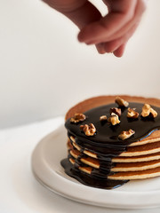 pancakes with dressing chocolate and nuts on white plate on white background